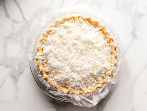 This image shows a vegan coconut meringue pie featuring a creamy coconut filling made with coconut milk, shredded coconut, and a meringue topping sprinkled with toasted coconut shavings, served as a delightful dessert.