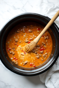 This image shows cream cheese being whisked into the soup in the crockpot, creating a creamy and smooth texture.