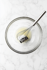 This image shows a small bowl with dressing ingredients, including soy sauce, vinegar, and sesame oil, being whisked together until smooth and well combined.