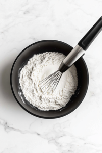 this image shows Flour being whisked into melted vegan butter in the pot, forming a roux that will thicken the creamy garlic sauce for the pasta.