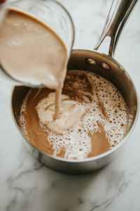 This image shows infused almond milk being whisked into a roux, blending into a velvety smooth vegan béchamel sauce for the lasagna.