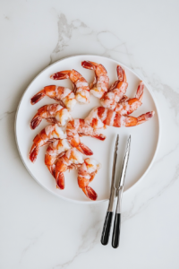 This image shows sauced shrimp being carefully wrapped with halved slices of bacon, creating a savory and indulgent bite-sized treat.