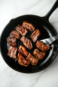 This image shows slices of bacon sizzling in a skillet, cooking until crispy and ready to add a savory crunch to the Steak Cobb Salad.