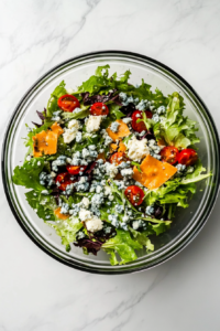 This image shows blue cheese crumbles being sprinkled over the salad, providing a tangy optional topping to the Steak Cobb Salad.