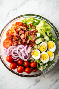 This image shows thinly sliced avocado being layered over the salad base, adding a creamy and nutritious element to the Steak Cobb Salad.