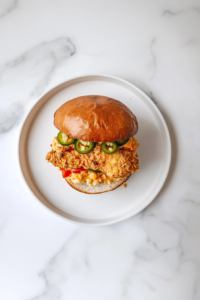 This image shows a perfectly assembled Honey Pepper Pimento Chicken Sandwich, served on a plate with golden toasted buns and flavorful toppings.