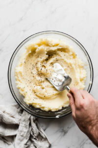 This image shows butter, milk, and seasonings being mixed into mashed potatoes, creating a flavorful and creamy topping.