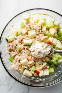 This image shows mayonnaise being added to the tuna salad mixture, followed by a final mixing to create a creamy and well-combined dish.