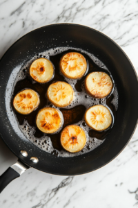 This image shows small stacks of layered potatoes being carefully placed into a hot pan of oil, beginning the frying process.