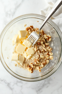 This image shows chunks of butter and chopped walnuts being added to the dry mixture, creating a crumbly, rich topping for the Crockpot Apple Crisp.