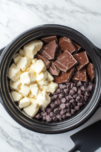 This image shows large chunks of chocolate being added into a slow cooker, the first step in creating creamy and rich crockpot peanut clusters.