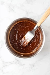 This image shows condensed milk being poured into the heated sugar and glucose mixture, creating a rich and creamy base for the glaze.