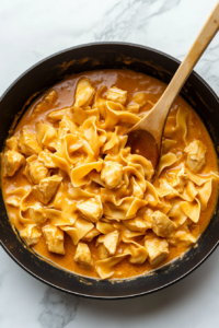 This image shows cooked noodles and shredded chicken being added to the creamy sauce in the skillet, bringing all the flavors together.