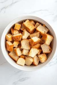 This image shows cubed bread pieces being added to the crockpot, forming the base for the French toast before the egg mixture is poured over.