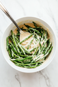 This image shows fresh green beans being added to the creamy mixture of mushroom soup, milk, and seasonings, ready to be combined for the Crockpot green bean casserole.