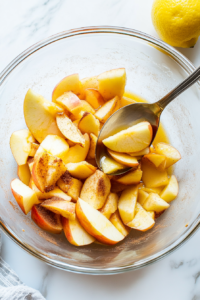 This image shows fresh lemon juice being added to the sliced apples, brightening the flavors and enhancing the taste of the filling for the apple crisp.