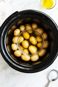 This image shows raw potatoes and seasonings being added into a slow cooker, setting the foundation for a flavorful crockpot potato dish.