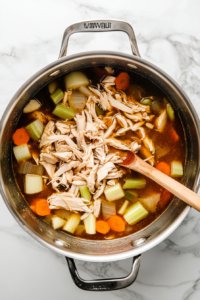 This image shows shredded chicken being returned to the pot of simmering soup, enriching the broth with its flavor and texture.