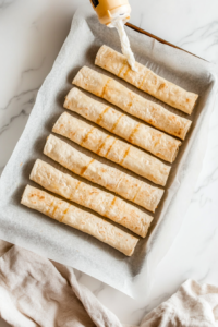 This image shows a tray of potato-filled taquitos being baked in the oven until golden brown and crispy.