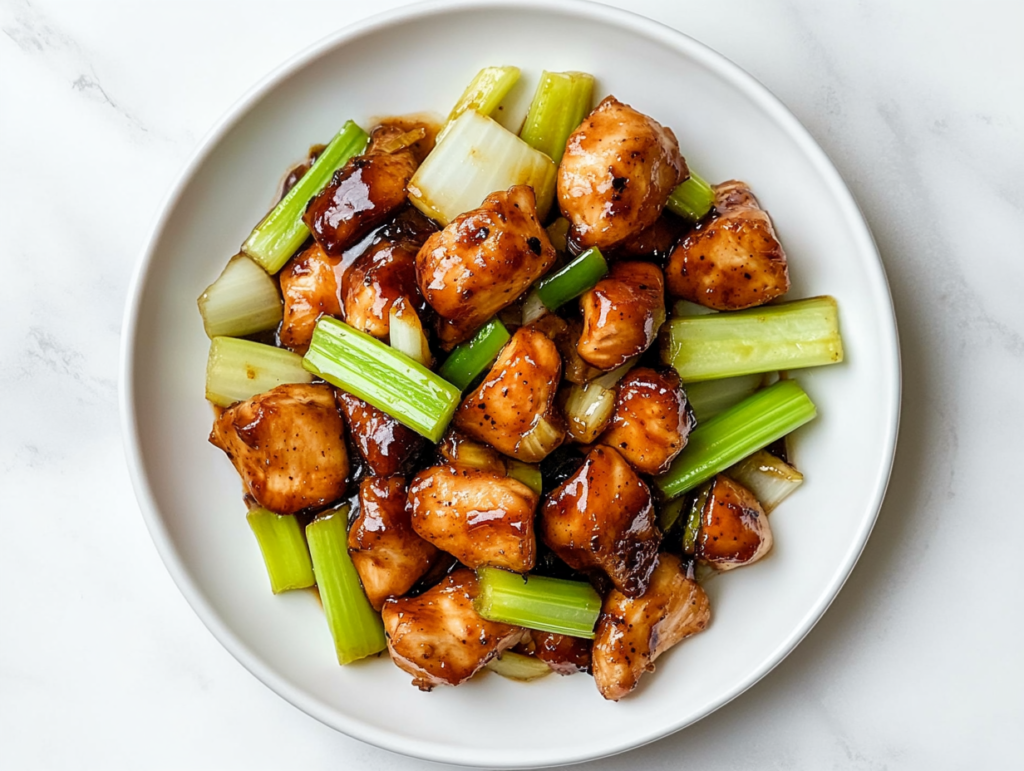 This image shows a plate of Black Pepper Chicken Panda Express, featuring glazed chicken pieces, celery stalks, and onions, served on a white round plate.