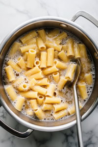 This image shows rigatoni pasta boiling in a large pot of salted water, cooking to a perfect al dente texture for a rich and creamy shrimp rigatoni dish.