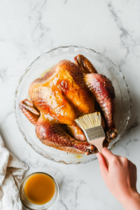 This image shows a brush generously coating the smoked turkey breast with melted butter, enhancing its richness and creating a glistening finish.