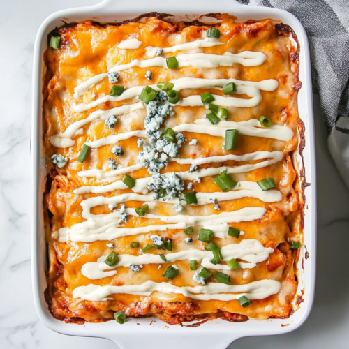 This image shows a freshly baked Buffalo Chicken Lasagna in a white rectangular dish, topped with a drizzle of ranch dressing, sliced green onions, and blue cheese crumbles.