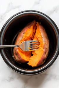 This image shows a fork piercing a slow-cooked sweet potato, testing its tenderness to ensure it is fully cooked and ready to serve.