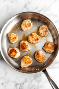 This image shows chicken medallions sizzling in a pan, cooking to a golden brown on the first side.