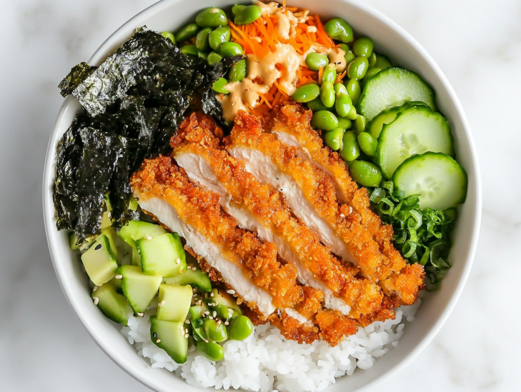 This image shows a beautifully arranged chicken katsu rice bowl with a base of fluffy rice, topped with crispy chicken katsu, fresh cucumber, avocado slices, pickled ginger, green onions, and nori, served in a white bowl.