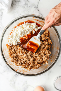 This image shows ground turkey being mixed with seasonings and breadcrumbs in a bowl to create the meatloaf base for the casserole.