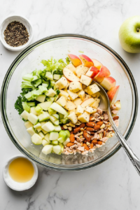 This image shows all the prepped ingredients, including tuna, apples, and vegetables, being mixed together in a large bowl to form the base of the salad.