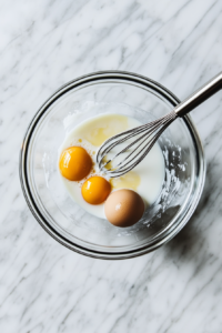 This image shows a bowl of wet ingredients, including eggs, milk, and melted butter, being whisked together to create a smooth mixture for the cornbread batter.