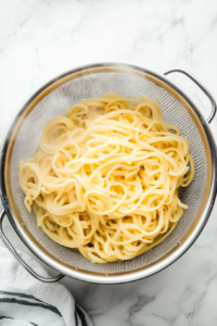 This image shows cooked pasta being drained in a colander, ready to be added to the soup just before serving.