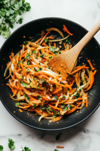 This image shows finely chopped carrots, ginger, and garlic being stirred with curry powder in a hot pan, creating a fragrant and flavorful base for the dish.