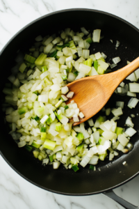 This image shows onions, garlic, and celery being sautéed in a pot, releasing their aroma and forming the flavorful base of the soup.