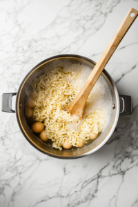 This image shows egg noodles being cooked in a pot of boiling water until tender, forming the base for the skillet dish.