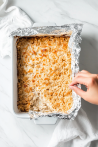 This image shows a prepared breakfast casserole covered with plastic wrap, ready to be refrigerated overnight to allow flavors to meld together.