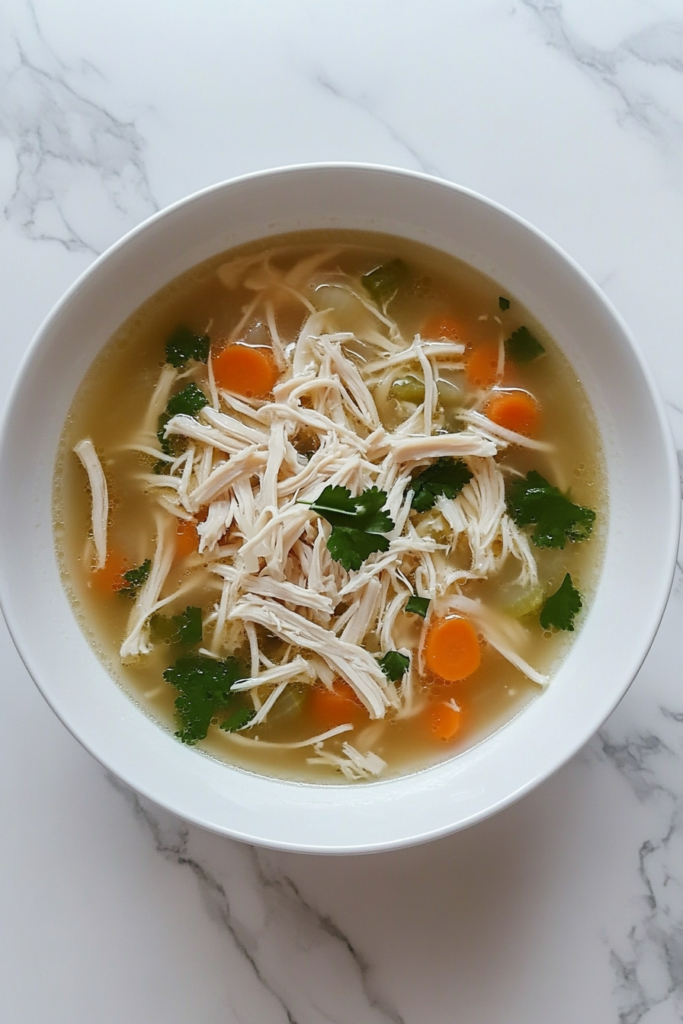 This image shows a comforting crockpot chicken noodle soup, filled with tender shredded chicken and bright orange carrot slices, served warm in a white round bowl.