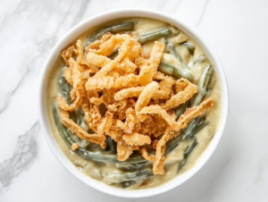 This image shows Crockpot green bean casserole served in a white bowl, mixed with creamy mushroom soup, milk, salt, and pepper until fully blended, creating a rich and savory dish.