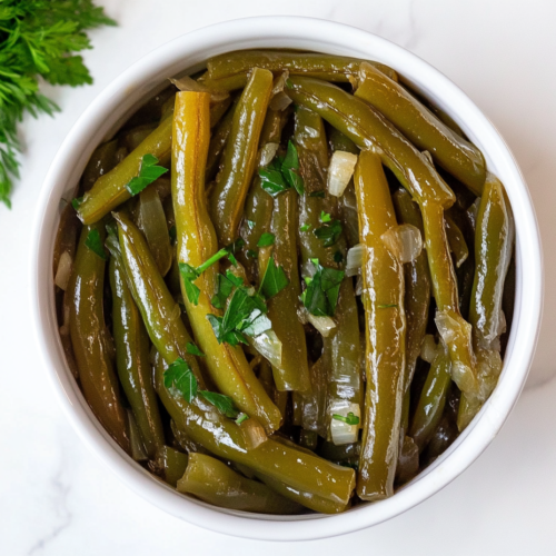 This image shows crockpot green beans served in a white round bowl, tossed in a flavorful mix of chicken broth, garlic, and butter, and topped with freshly chopped cilantro for a vibrant finish.