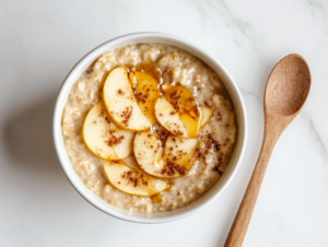 This image shows crockpot oatmeal served in a white bowl, topped with fresh apple slices, with a spoon placed beside it, ready to be enjoyed for a wholesome breakfast.