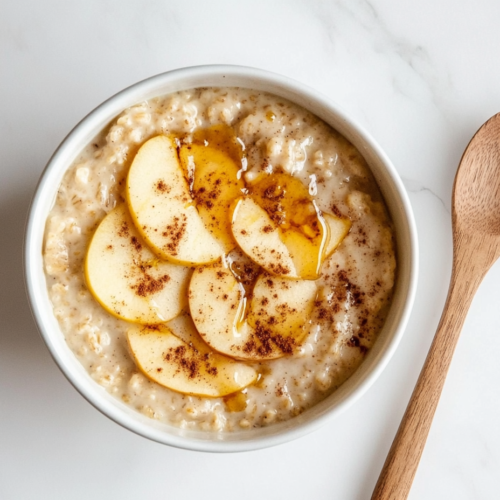 This image shows crockpot oatmeal served in a white bowl, topped with fresh apple slices, with a spoon placed beside it, ready to be enjoyed for a wholesome breakfast.