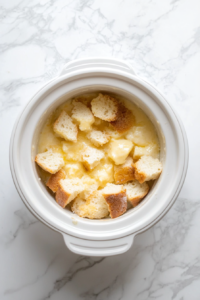 This image shows the crockpot filled with the French toast mixture resting in the refrigerator, allowing the bread to fully soak up the custard for a rich flavor.