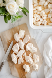 This image shows raw chicken pieces being carefully cut and arranged in a casserole dish, ready for the creamy sauce and toppings.