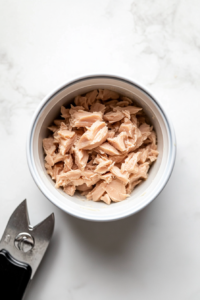 This image shows canned tuna being drained of excess liquid, ensuring the fish is prepared and ready to be mixed into the tuna salad.