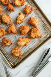 This image shows freshly fried chicken pieces resting on a wire rack, allowing excess oil to drain for a lighter and crispier texture.