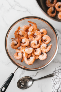 This image shows freshly boiled shrimp being carefully poured into a colander, allowing excess water to drain away while preserving their plump, juicy texture.