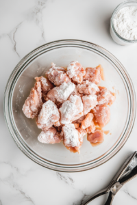 This image shows pieces of marinated chicken being coated in cornstarch, creating a light and crispy exterior when fried.