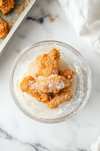 This image shows marinated chicken being dredged in a seasoned flour mixture, creating a thick, crispy coating.